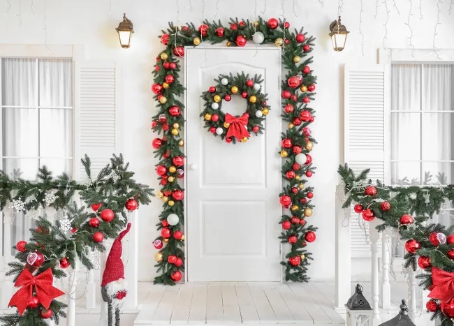 Christmas-decorated white porch with garland, ornaments, wreath on the door, and lights.